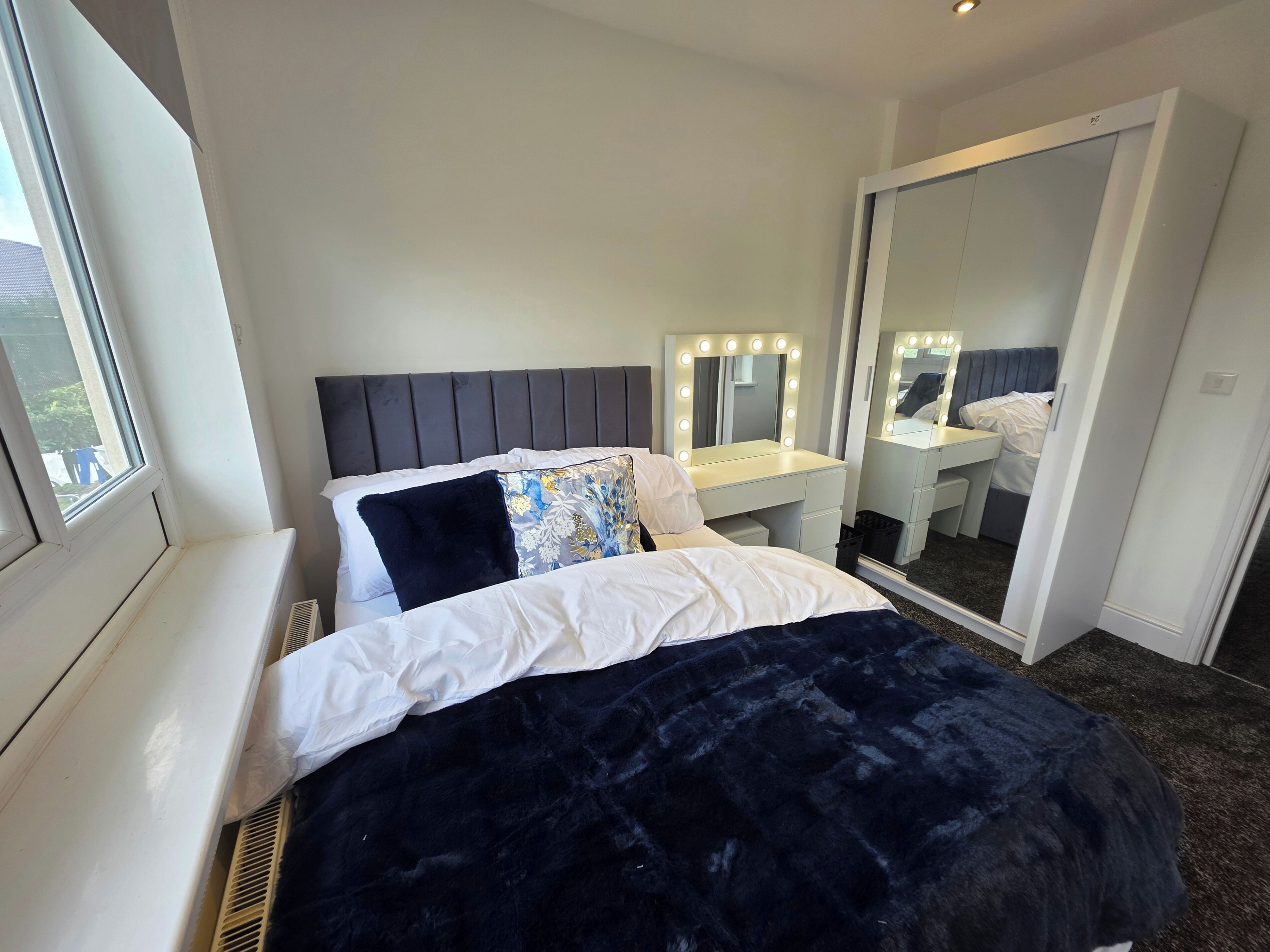 A bedroom with a bed, a vanity with a mirror and lights, and a walk-in closet.