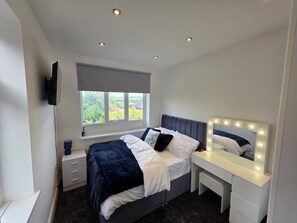 A bedroom with a bed, bedside table, mirror with lights, window, and ceiling lights. - 5 Beds, 7 Guests, Private Garden, Free Parking (Nottingham)