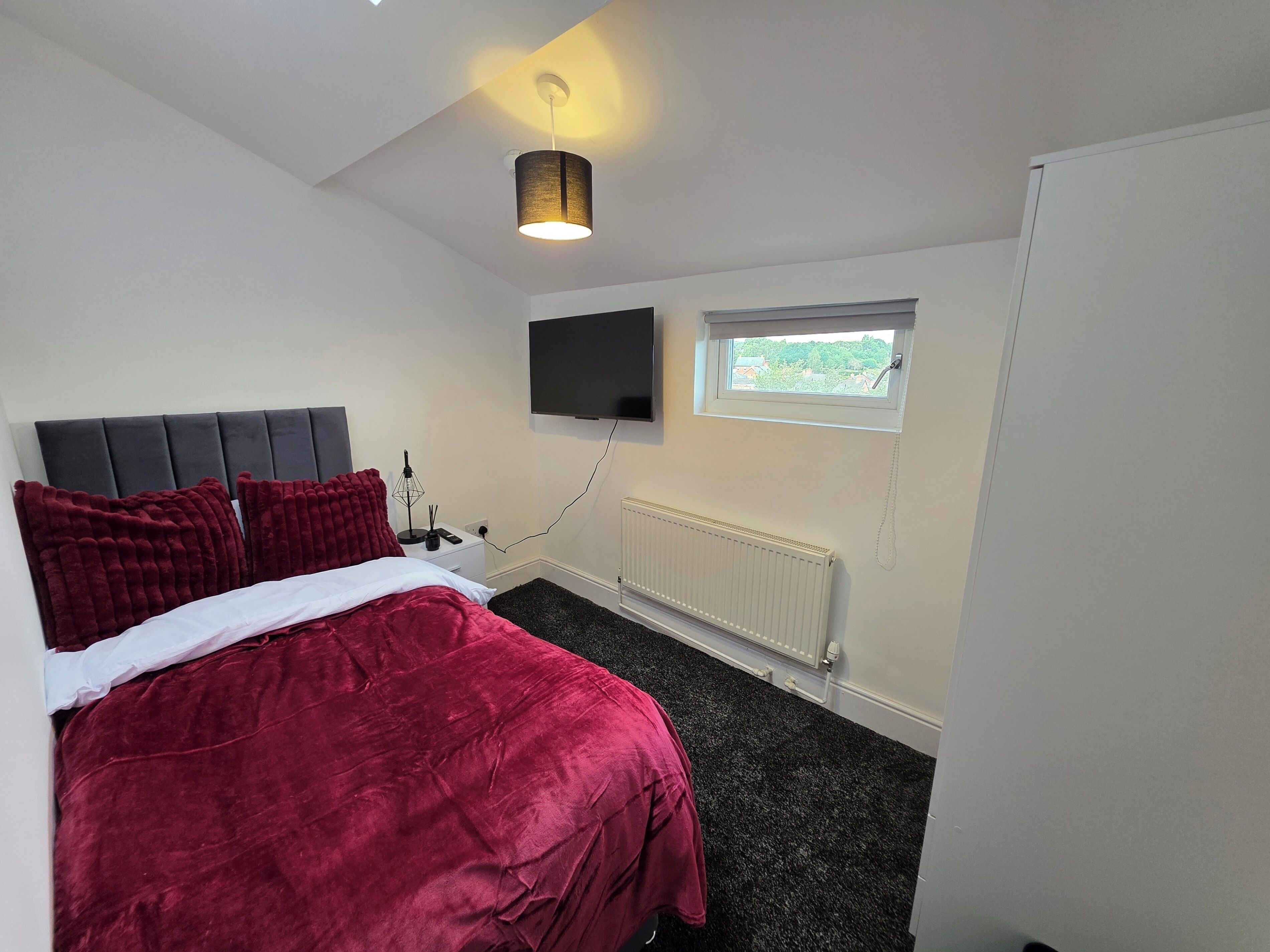 A bedroom with a bed, a flat-screen TV, a window, and a radiator.