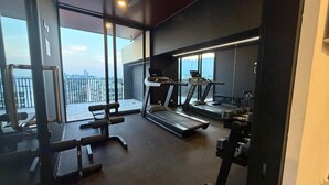 A gym with treadmills, weight machines, and a bench. It has large windows with a view of the city.