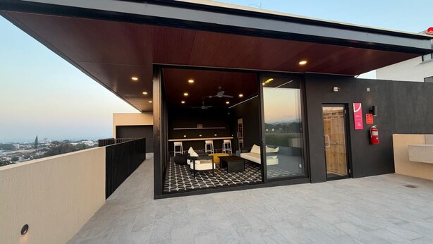 A modern outdoor lounge area with a glass door leading to an interior space, a ceiling fan, and a fire extinguisher.