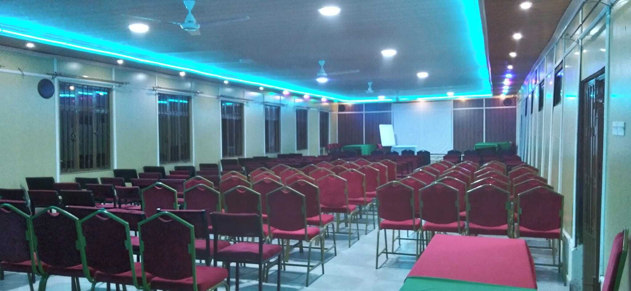 Un salón de conferencias con filas de sillas rojas y una zona de escenario.