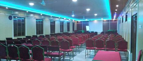 Un salón de conferencias con filas de sillas rojas y una zona de escenario.