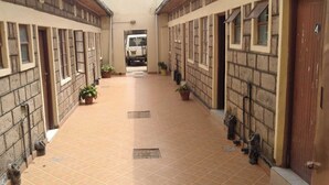 Un couloir au sol carrelé, agrémenté de plantes en pot et bordé de portes des deux côtés.