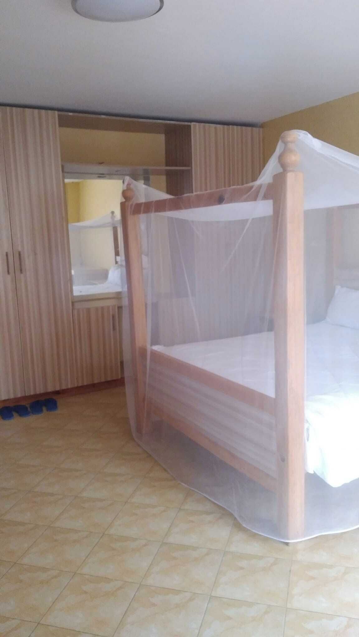 Habitación con cama con dosel, un armario y baño visible a través de una puerta abierta.