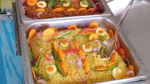 Un buffet proposant divers plats, notamment du riz aux légumes et aux œufs, et une personne se tenant à l’arrière-plan.