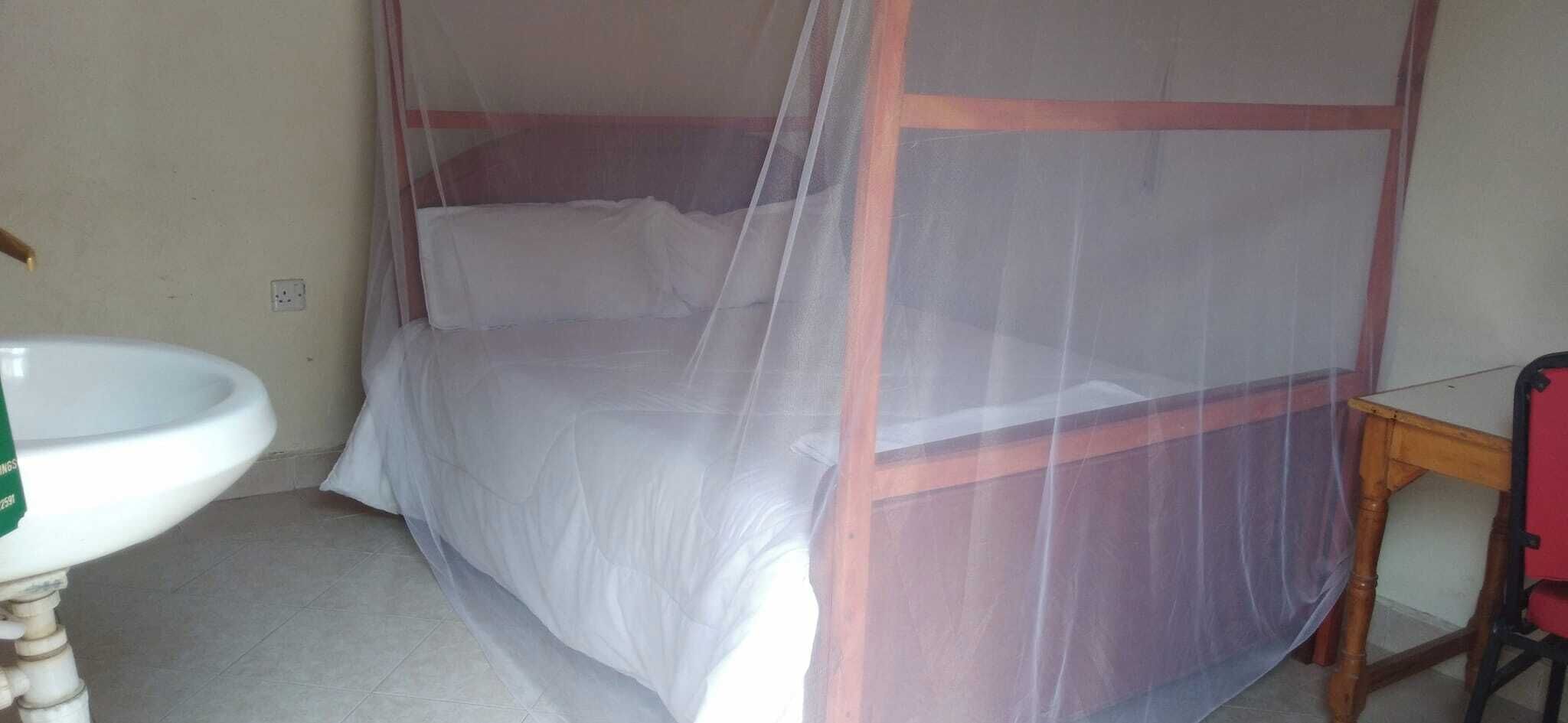 A room with a bed under a mosquito net, a wooden chair, a white sink, and a tiled floor.