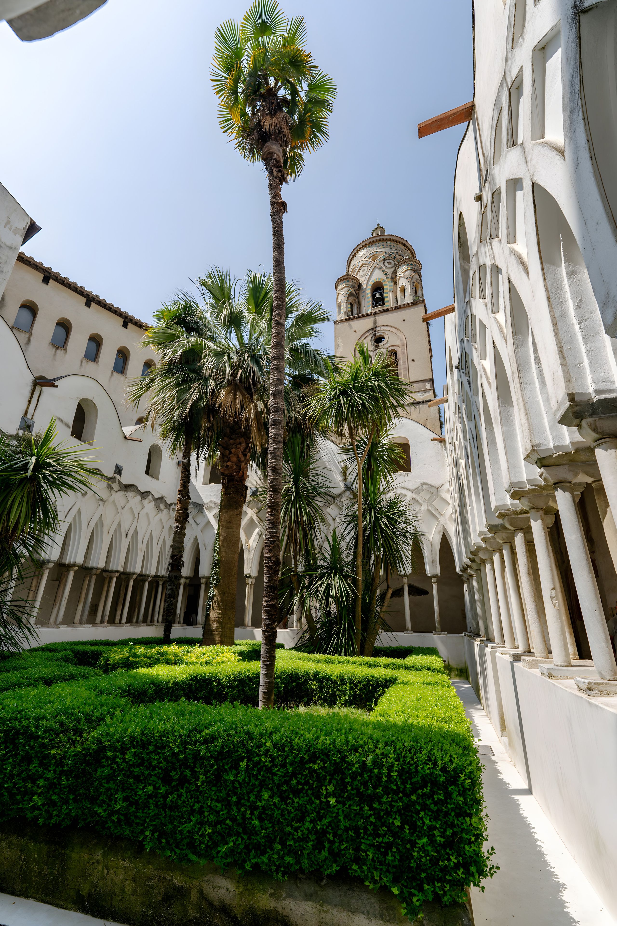 A courtyard with palm trees, a fountain, and a building with a bell tower.
