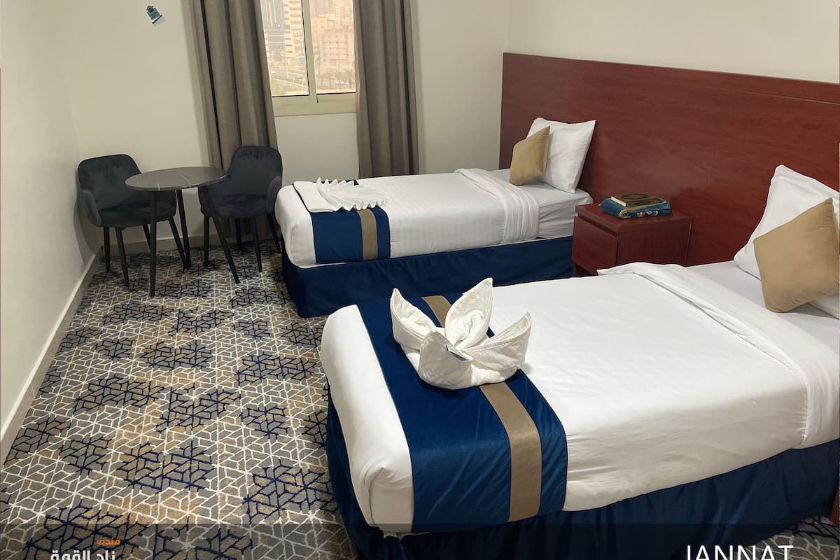 Hotellihuone, jossa on kaksi sänkyä, pieni pöytä ja tuoli.