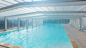 An indoor swimming pool with clear glass walls, a tiled floor, and a row of chairs along the side.
