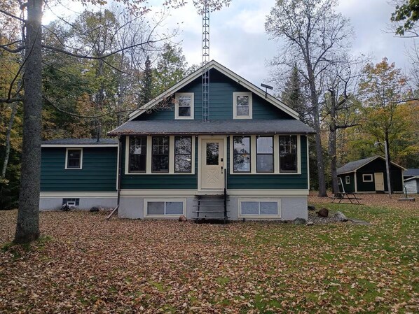 A two-story house with a front porch, a chimney, and a small shed in the background.