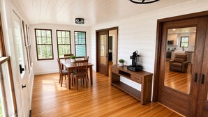 A spacious room with wooden flooring, a dining table with chairs, a wooden console table, and a large mirror.