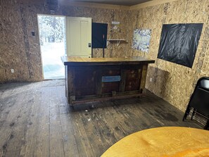 A room with a wooden floor, a central wooden counter, and a door leading outside.