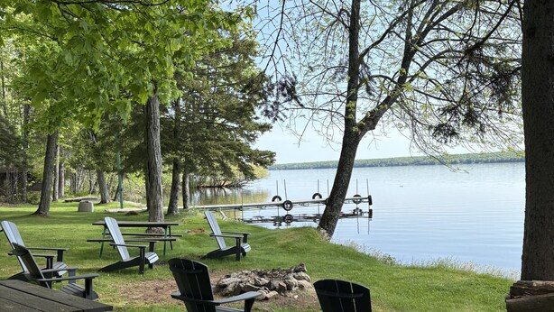 A lakeside picnic area with Adirondack chairs, picnic tables, and a fire pit.