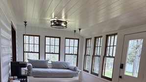 A room with a wooden floor, a dining table, a sofa, and a hanging light fixture.