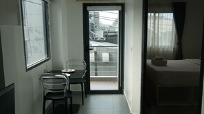 A small, narrow room with a bed, a table with chairs, and a window.