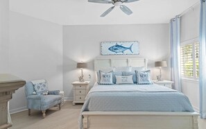 A bedroom with a bed, a chair, a nightstand, a ceiling fan, and a window with curtains.