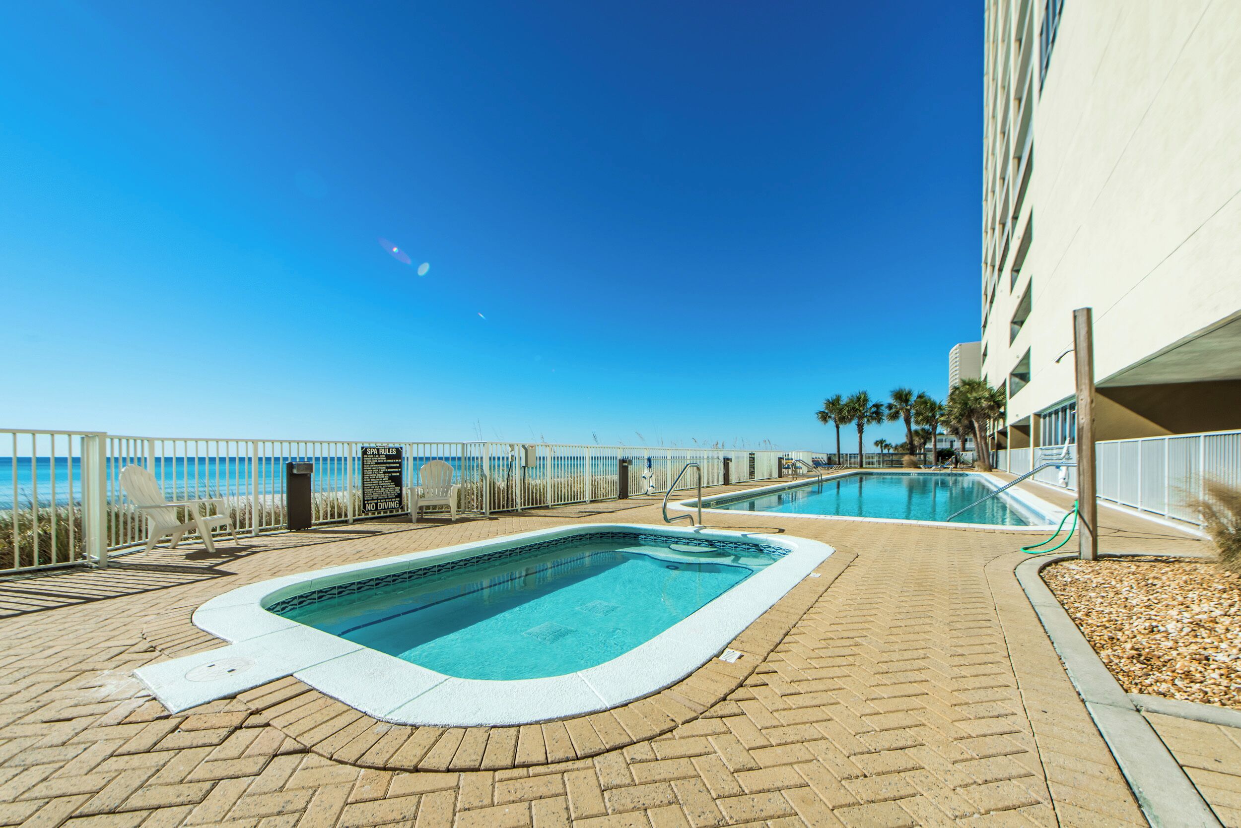 Área da piscina com vista para o mar, uma espreguiçadeira e uma placa indicando que não é permitido nadar.