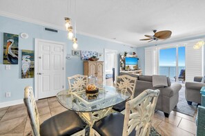 A living room with a glass-top dining table, white wicker chairs, a grey sofa, and a ceiling fan. - 🏖️BeachFront-Balcony-Heated Pool-Ocean Reef 1105🏖️ (Panama City Beach)