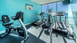 Une salle de sport équipée d’appareils de cardio, d’un téléviseur fixé au mur et d’une grande fenêtre donnant sur l’océan.