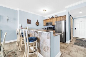 A kitchen with a central island, wooden cabinets, a stainless steel refrigerator, and a microwave.