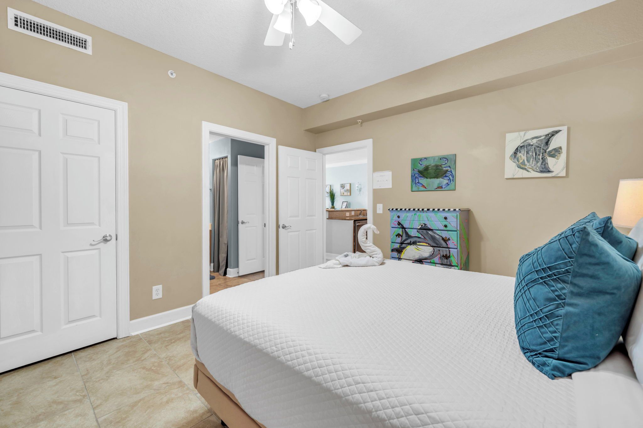 Quarto com cama, ventilador de teto, porta e banheiro visível através de uma porta aberta.