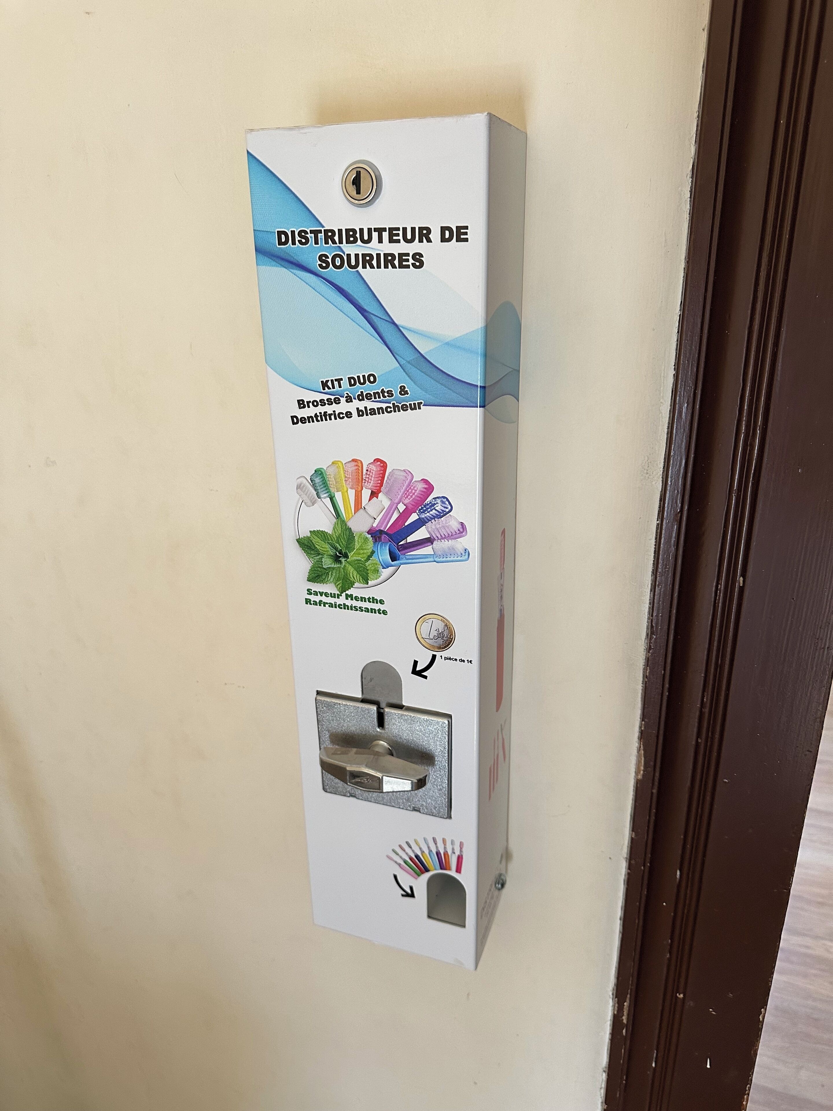 Een wandbevestigde dispenser met hendel, muntgleuf en een slot.
