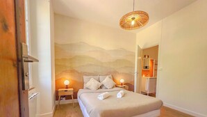 A bedroom with a bed, two bedside tables with lamps, a wall mural, and a bathroom visible through an open door.