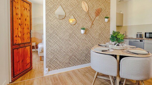 A modern kitchen with a herringbone-patterned backsplash, a dining area with a round table, and a wooden door.