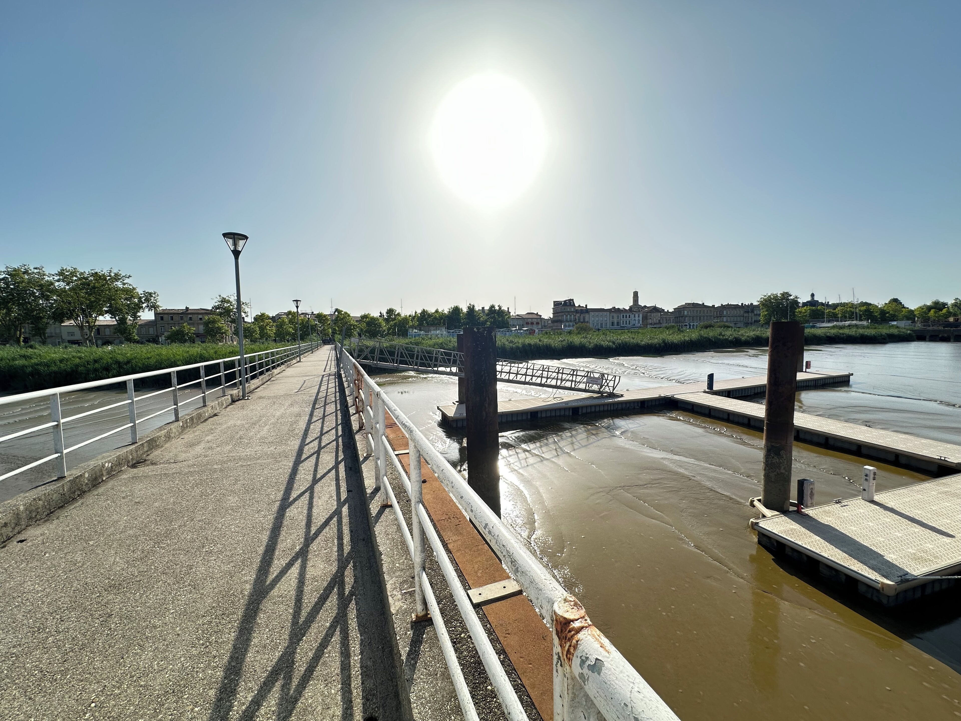 A bridge with a metal railing and a concrete walkway leading to a water body.
