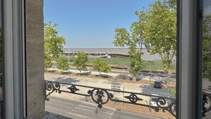 A view from a window with a metal railing, overlooking a parking lot with trees and a distant building.