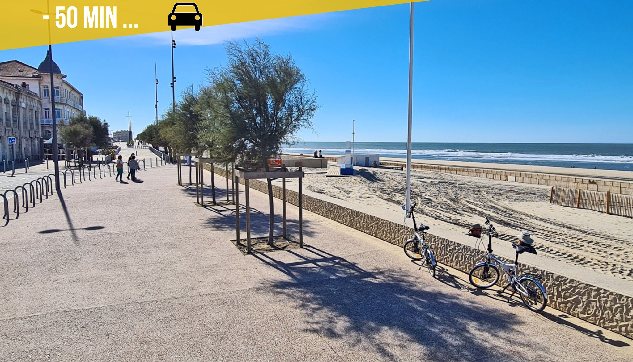 Un paseo marítimo costero con cielo despejado, una playa de arena y una fila de bicicletas estacionadas a lo largo del sendero.