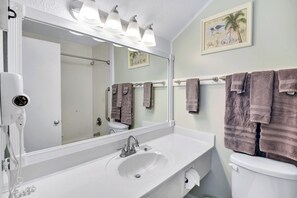 A bathroom with a white sink, a mirror, a toilet, and a towel rack with multiple towels. - Villa 459: 3 BR, 2 BA Condominium in Jekyll Island, Sleeps 6 (Jekyll Island)