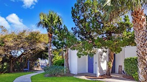 A pathway leading to a building with a blue door, surrounded by greenery and palm trees. - Villa 376 - Driftwood Cottage (Jekyll Island)