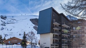 A modern building with multiple balconies and a ski resort in the background.