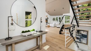 A modern living room with a wooden staircase, a round mirror, and a console table with decorative items.
