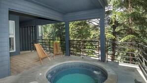 A covered outdoor hot tub area with two wooden lounge chairs and a stone-tiled pool.