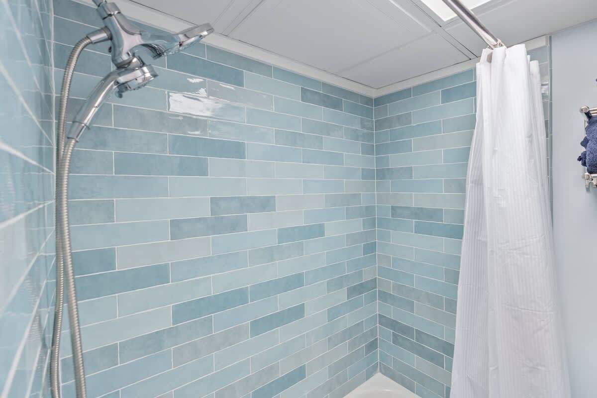 A bathroom with blue-tiled walls, a shower with a handheld showerhead, and a white shower curtain.