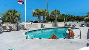 Ein Pool mit Liegestühlen, Palmen und Flaggen.