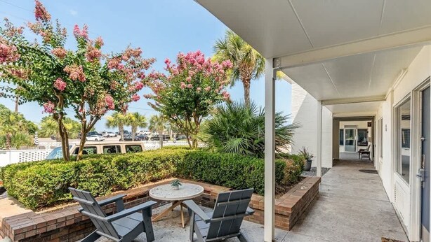 Eine überdachte Terrasse mit Tisch und Stühlen, umgeben von üppiger Vegetation und blühenden Bäumen.