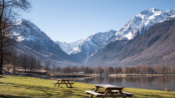 A lakeside picnic area with benches, surrounded by mountains and a clear sky.