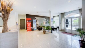 A modern hotel lobby with a reception desk, seating area, and large windows.
