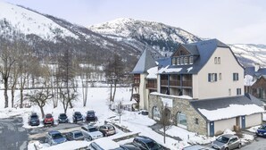 A multi-story building with a ski lodge sign, surrounded by snow-covered parking and a mountainous backdrop.