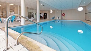 An indoor swimming pool with clear water, surrounded by white lounge chairs and a tiled floor.