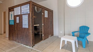 A small, wooden, enclosed bathroom with multiple signs in French, a white plastic chair, and a blue plastic chair.
