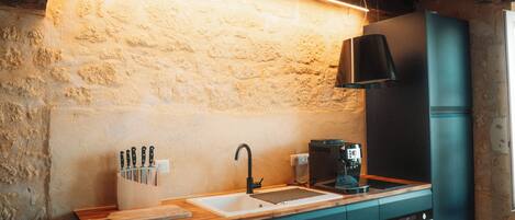 A kitchen with a wooden ceiling, a stone wall, and a modern appliance.