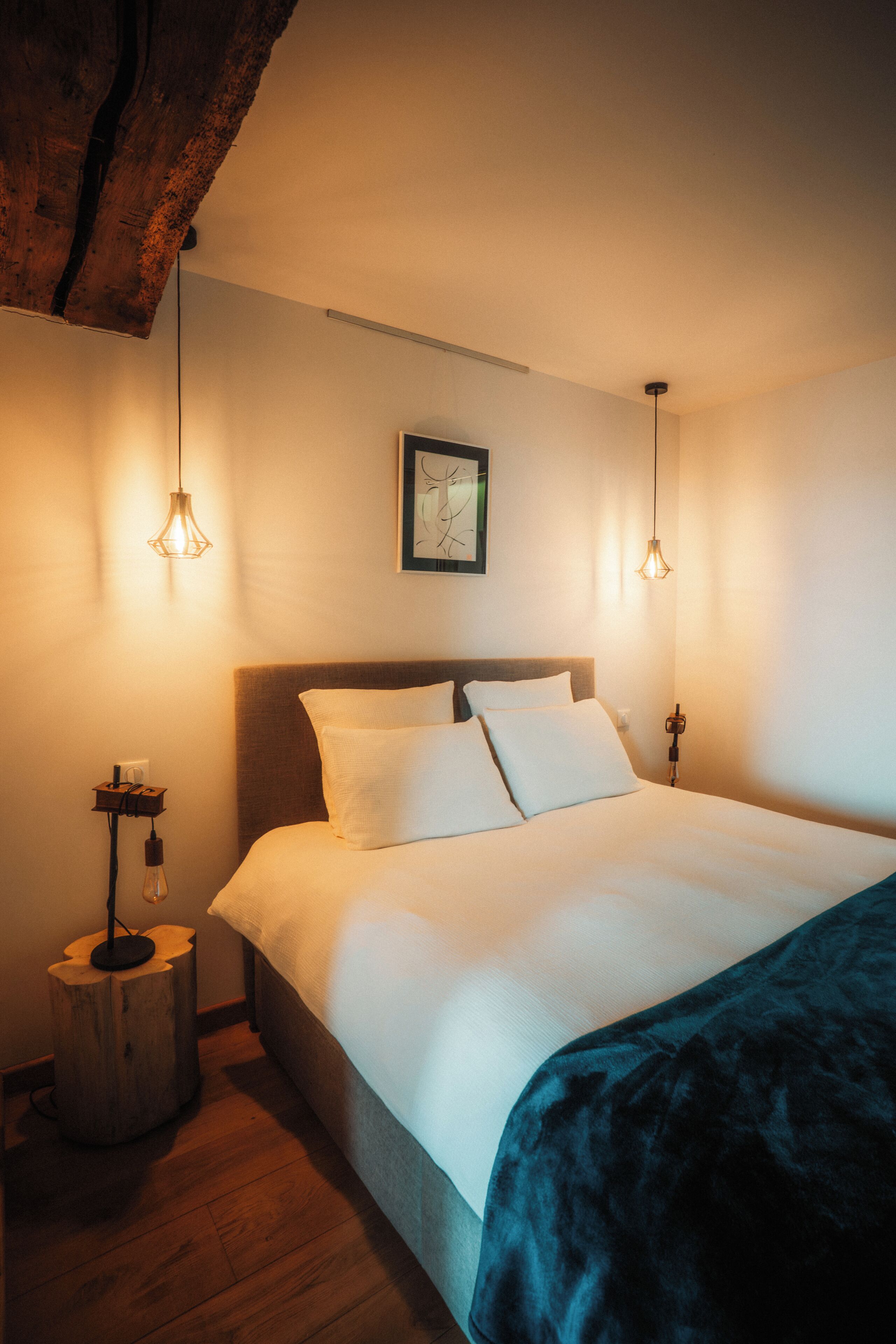 A bedroom with a large bed, two bedside lamps, a wooden nightstand, and a framed picture on the wall.