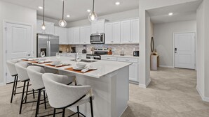 A modern kitchen with white cabinetry, a large island with bar stools, stainless steel appliances, and pendant lighting.