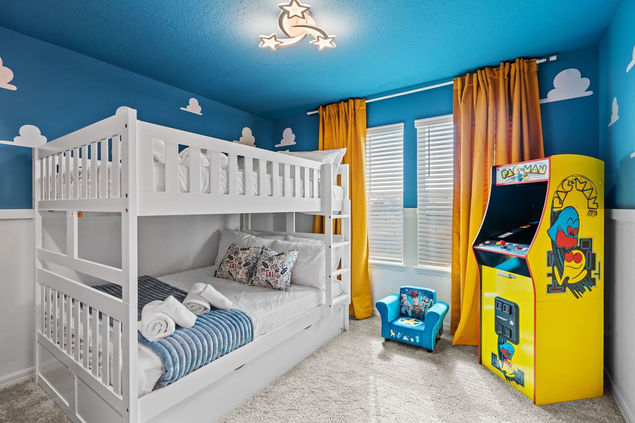 A child's bedroom with bunk beds, a Pac-Man arcade machine, and a window with curtains.