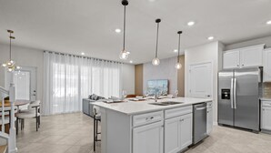 A modern kitchen with white cabinetry, a central island, stainless steel appliances, pendant lighting, and a dining area with a white table and chairs.
